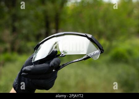 mano en guantes médicos negros sostiene gafas médicas en un fondo aislado Foto de stock