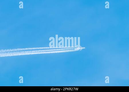 Disparo de un avión a reacción en lo alto de los cielos azules. El avión en el cielo azul deja rastros aéreos. Viajar en aviones. Foto de stock