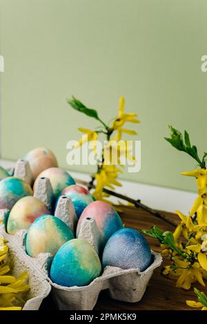 Huevos de Pascua coloridos sobre un fondo verde junto a flores amarillas Foto de stock