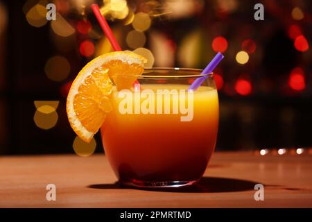 Copa de sabroso Tequila Sunrise con rodaja naranja en la mesa contra luces borrosas Foto de stock