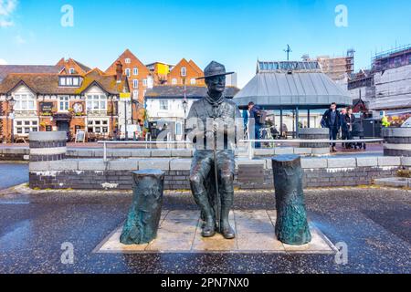 Estatua de bronce de Robert Baden-Powell, el fundador de la asociación de exploradores en el muelle en el puerto de Poole se representa sentado en un tronco de árbol Foto de stock