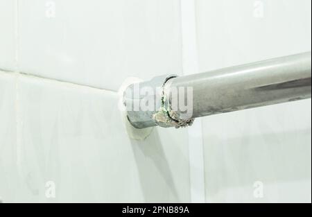 Fuga de agua del toallero calentado en lugares de conexiones roscadas en el fondo de baldosas blancas. Foto de stock