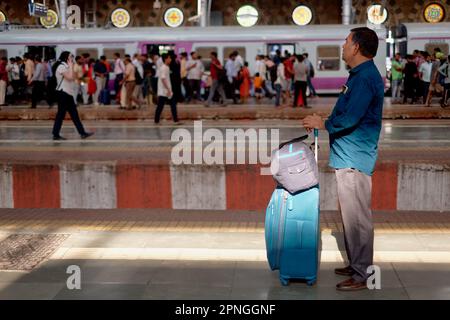 Un pasajero con equipaje esperando un tren suburbano en Chhatrapati Shivaji Maharaj Terminus, Mumbai, India Foto de stock