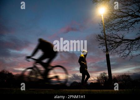 Un ciclista recorre un parque de Londres al atardecer luz de calle Foto de stock