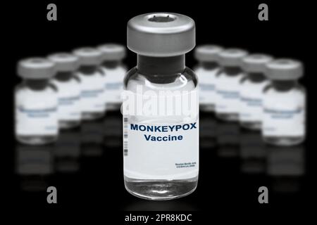 Vacuna de la monkeypox primer plano sobre un fondo de espejo negro. En el fondo hay viales de vacuna borrosas Foto de stock