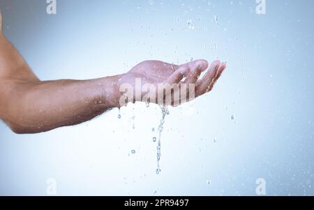 Lávese las manos, disminuya los gérmenes. Fotografía de estudio de un hombre irreconocible sosteniendo su mano bajo el agua corriente sobre un fondo gris. Foto de stock