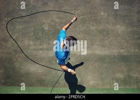 Un poco de calentamiento. Disparo en ángulo alto de un joven enfocado usando una cuerda de salto como ejercicio fuera en una cancha de tenis durante el día. Foto de stock