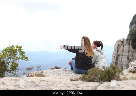Dos excursionistas contemplando la naturaleza sentado en un acantilado y señalando lejos Foto de stock