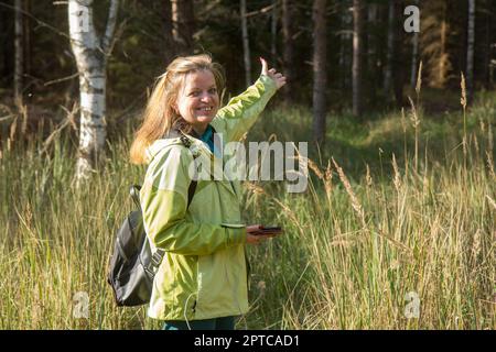 Una mujer con su teléfono móvil en el bosque. Jugando al geocaching. Foto de stock