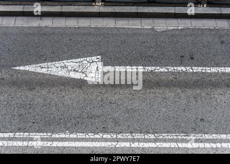 Vista general de una flecha y líneas divisorias de tráfico en asfalto agrietado Foto de stock