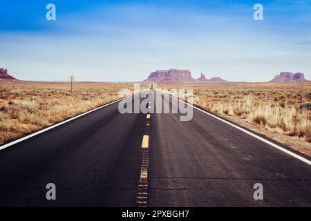 Solitario y desierto camino americano en el desierto del valle del monumento sin coches, mostrando punto de fuga. Foto de stock