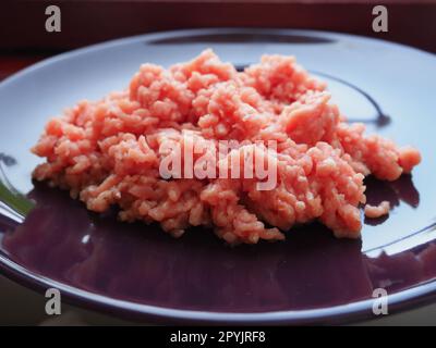 Carne picada en un plato grande de cerámica púrpura. Deliciosa carne molida fresca para hacer chuletas, filetes, hamburguesas, albóndigas. Productos semielaborados de cerdo Foto de stock