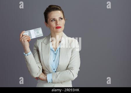 pensativo elegante de mediana edad dueña de pequeña empresa mujer en un traje de negocios ligero con paquetes de dinero de dólares aislados en gris. Foto de stock