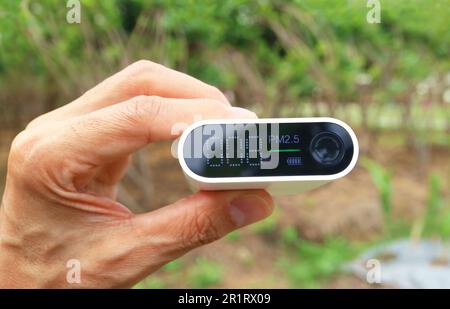 Mano del hombre sosteniendo un sensor de contaminación del aire que mide la calidad del aire en el jardín Foto de stock