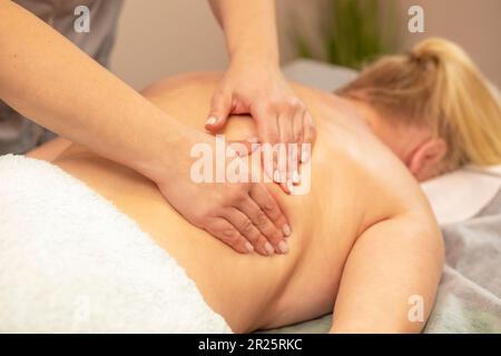 Masajista, terapeuta haciendo masaje terapéutico profesional en la espalda de la mujer con sobrepeso, amasando los músculos del cliente en el salón de spa. Mental, salud Foto de stock