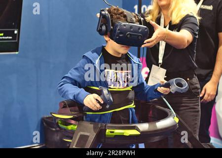 Un niño joven que juega una máquina inmersiva de la cinta de la realidad virtual con auriculares de 360 grados y almohadillas de control controladas a mano Foto de stock