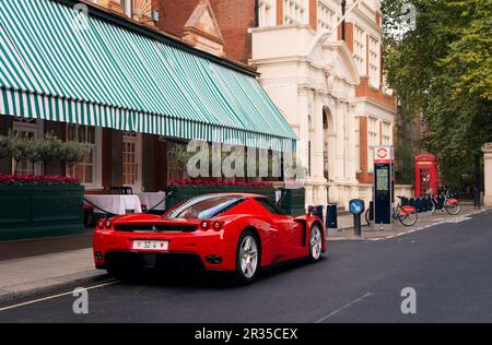 Un Ferrari Enzo rojo estacionado en una calle frondosa en Mayfair, Londres. Foto de stock