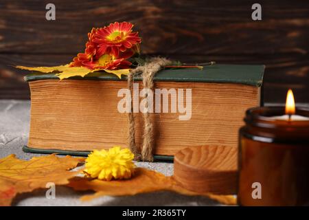Libro decorado con flores de crisantemo, hojas de otoño y vela perfumada en mesa con textura gris claro Foto de stock