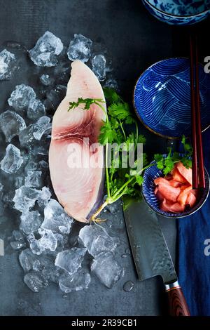 Filete de pez espada sobre hielo al lado del cilantro, un cuchillo y un tazón oriental Foto de stock