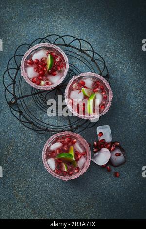 Gin y Tonic con semillas de granada en vasos con llantas azucaradas, hielo y limas Foto de stock