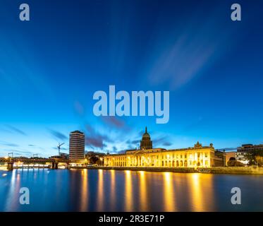 Vista iluminada de Custom House en la orilla del río Liffey bajo el horizonte azul, Dublín, Irlanda Foto de stock