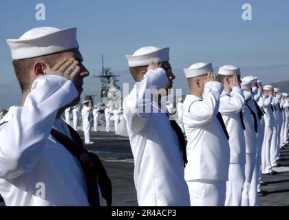 Los marineros de la Marina ESTADOUNIDENSE a bordo del portaaviones clase Nimitz USS Abraham Lincoln (CVN 72) rinden saludos a mano al USS Arizona Memorial en Pearl Harbor, Hawái, mientras manejan los rieles que se arrastran hacia el puerto Foto de stock