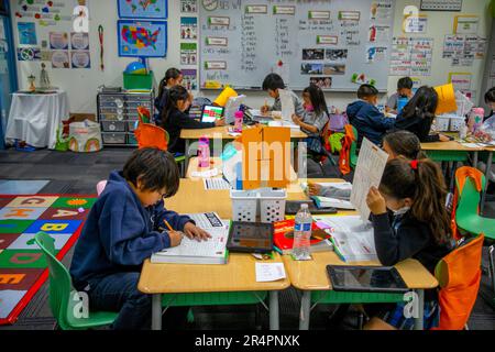 Los estudiantes multirraciales de primer grado trabajan en sus escritorios en una escuela primaria católica de California. Foto de stock