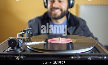 Hombre joven usando auriculares mientras que toca un disco de vinilo en un plato giratorio vintage Foto de stock