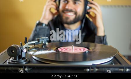 Hombre joven usando auriculares mientras que toca un disco de vinilo en un plato giratorio vintage Foto de stock