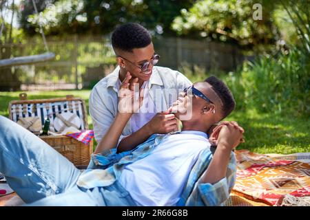 Feliz joven pareja de hombres gay abrazándose, disfrutando de picnic en el parque Foto de stock