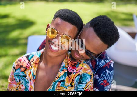 Feliz joven gay pareja masculina en gafas de sol abrazando Foto de stock