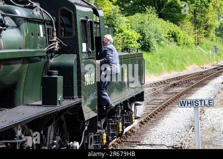 Conductor que sube a bordo de la locomotora de vapor de clase 2Mt estándar de 78022 BR conservada en el ferrocarril del valle Keighley & Worth en la estación Oxenhope, Reino Unido Foto de stock