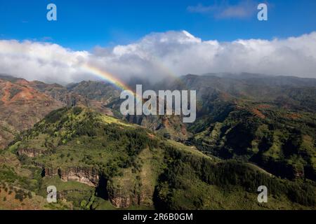 Una vista aérea de un arco iris sobre montañas verdes en el Parque Estatal Waimea Canyon en el condado de Kauai, Hawái Foto de stock
