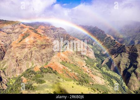 Una vista aérea de un arco iris sobre montañas verdes en el Parque Estatal Waimea Canyon en el condado de Kauai, Hawái Foto de stock