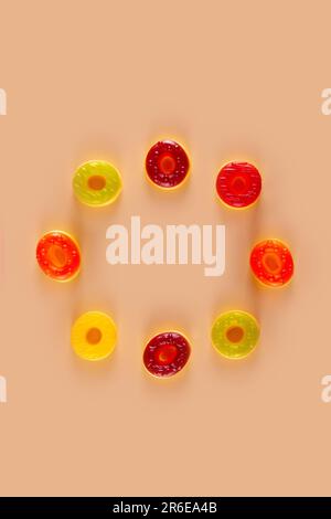 Círculo de caramelos redondos de jalea yacen sobre fondo naranja pastel. Exhibición colorida de círculos dulces Foto de stock