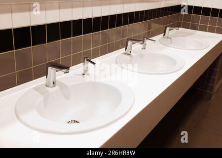 Fila de lavabos de cerámica limpios en el baño público Foto de stock
