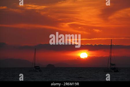 Una vista panorámica de los veleros que se deslizan a través de una tranquila masa de agua mientras el sol sale en el horizonte Foto de stock