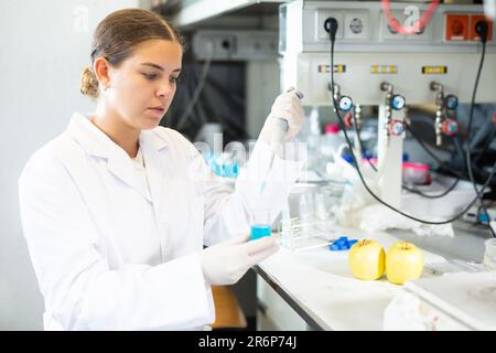 Investigador femenino inteligente en la mezcla de reactivos de capa blanca en tubo de ensayo con pipeta de laboratorio mientras trabaja en laboratorio Foto de stock