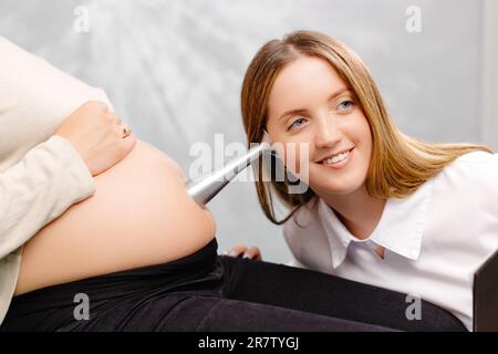 La mujer embarazada escucha los latidos del corazón y los movimientos del  bebé con un estetoscopio o un fetoscopio o un Pinard Horn. Salud fetal  prenatal, ansiedad, concepto del miedo. Fotografías de
