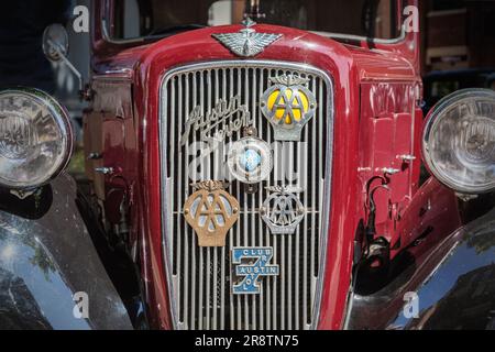Vista frontal detallada de un Austin Seven rojo de los años 1930 con varias insignias motorizadas en la rejilla del radiador. Austin Ruby en un show de coches clásicos y vintage. Foto de stock