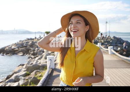 Hermosa señorita sonriente al aire libre. Retrato de mujer hispana alegre mirando al lado caminando en el paseo marítimo. Foto de stock