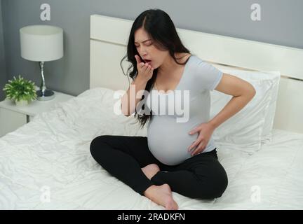 mujer embarazada enferma sintiéndose mal y tosiendo en una cama Foto de stock