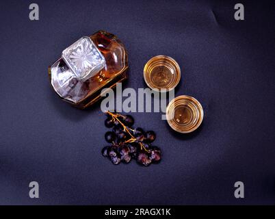 Un racimo de uvas oscuras y grappa en una botella de vidrio y dos vasos sobre un fondo negro. Vista superior, colocación plana. Foto de stock