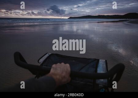 Hombre empujando el carro de bebé en la playa al atardecer Foto de stock