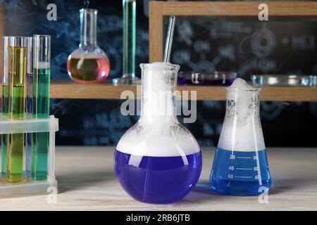 Cristalería de laboratorio con líquido azul sobre mesa de madera blanca. Reacción química Foto de stock