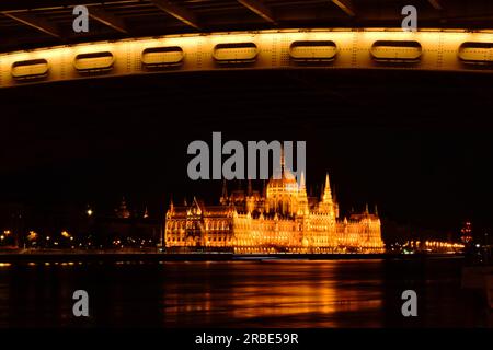 Vista panorámica de la noche del Parlamento en Budapest, Hungría. concepto de viaje y turismo. Reflexiones sobre las suaves aguas del Danubio bajo un puente. Foto de stock
