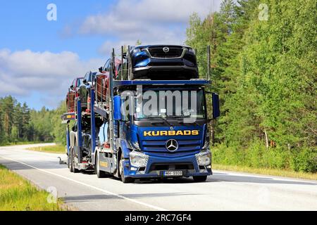 El camión portacoches Mercedes-Benz Actros azul de Kurbads transporta coches nuevos a lo largo de la carretera 25 en un día de verano. Raasepori, Finlandia. 7 de julio de 2023 Foto de stock