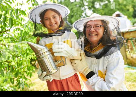 Retrato de apicultor femenino senior feliz con la muchacha que sostiene al fumador en el jardín del apiario Foto de stock