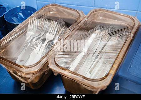Cajas de plástico con horquillas y cuchillos en la mesa de comedor de acero inoxidable - cubierto con película de plástico limpio Foto de stock