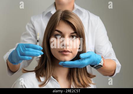 Retrato de una muchacha hermosa joven y la mano de una esteticista con una jeringa, inyecciones de belleza, mesoterapia, procedimientos faciales de la piel Foto de stock